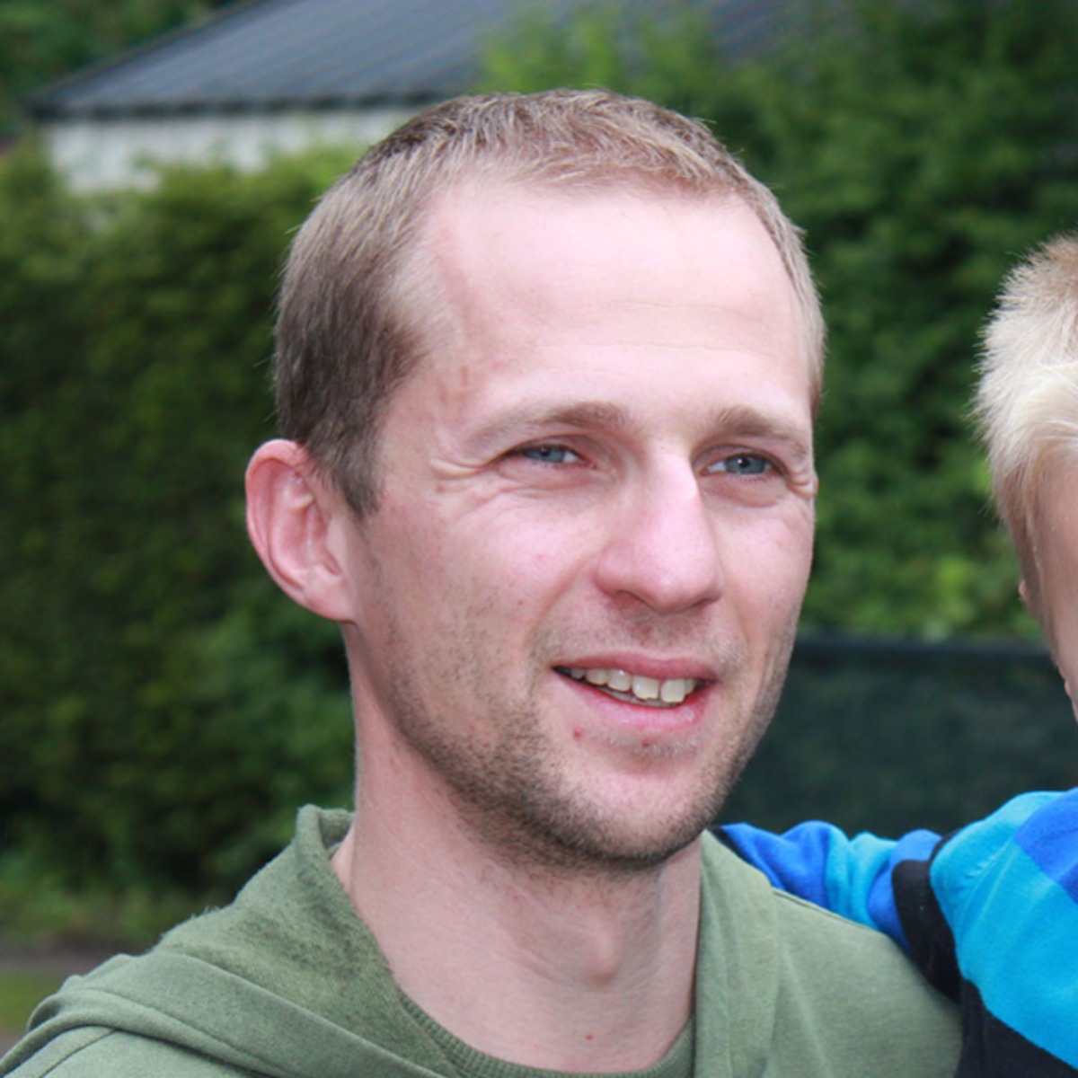 Bijgesneden portret van een man buiten met een groene achtergrond en zijn zoontje in de armen, een tevreden gebruiker van de Minimax waterontharder. 