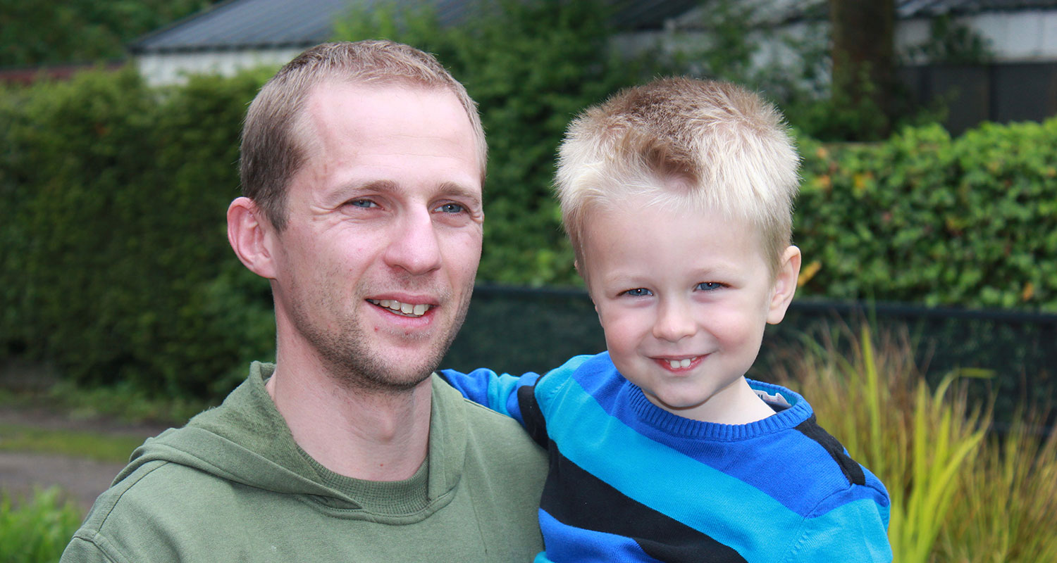 Portret van een man buiten met een groene achtergrond en zijn zoontje in de armen, een tevreden gebruiker van de Minimax waterontharder.