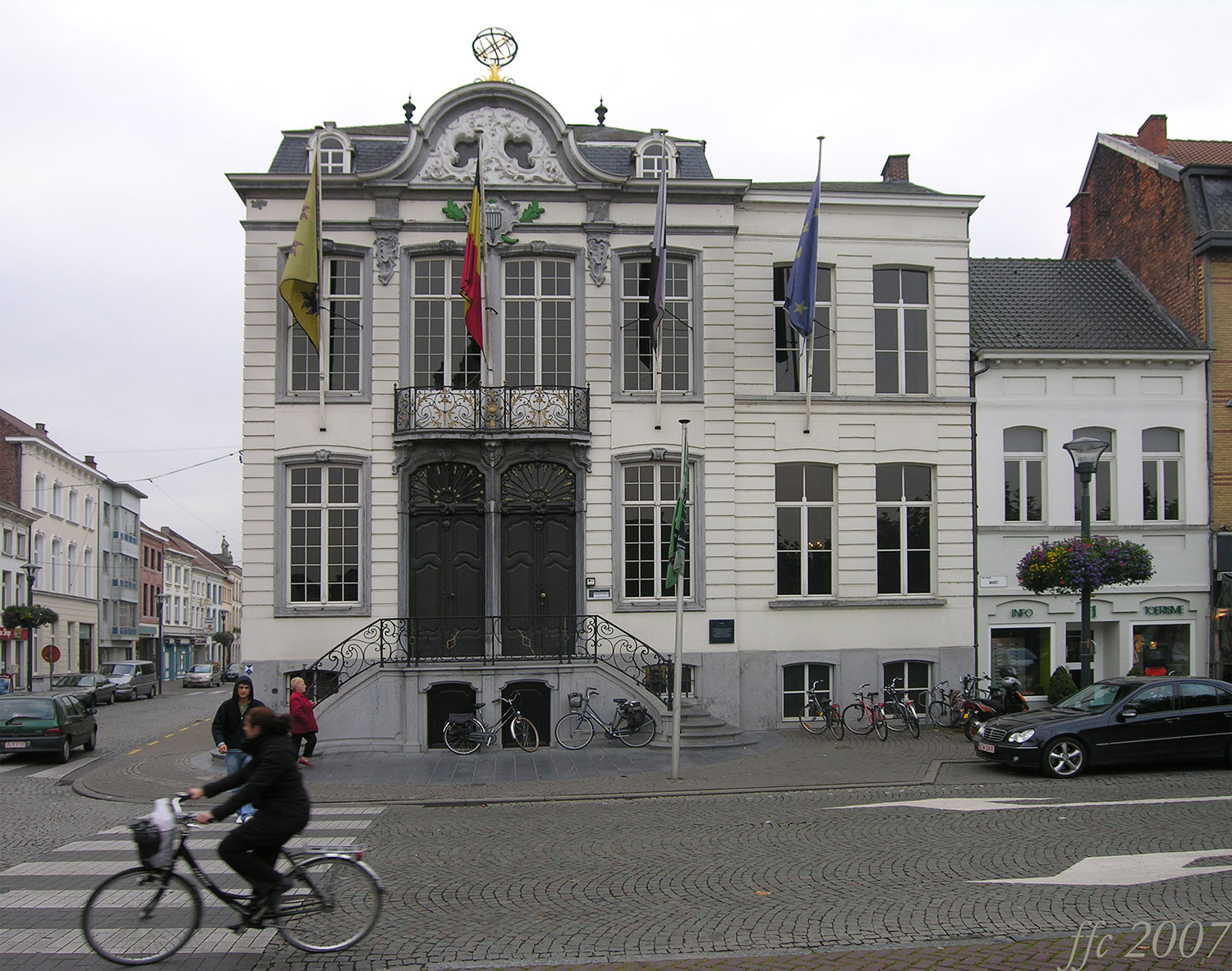 Fietser rijdt langs een historisch gebouw met meerdere vlaggen aan de gevel en verwijzing naar de Minimax waterontharder.
