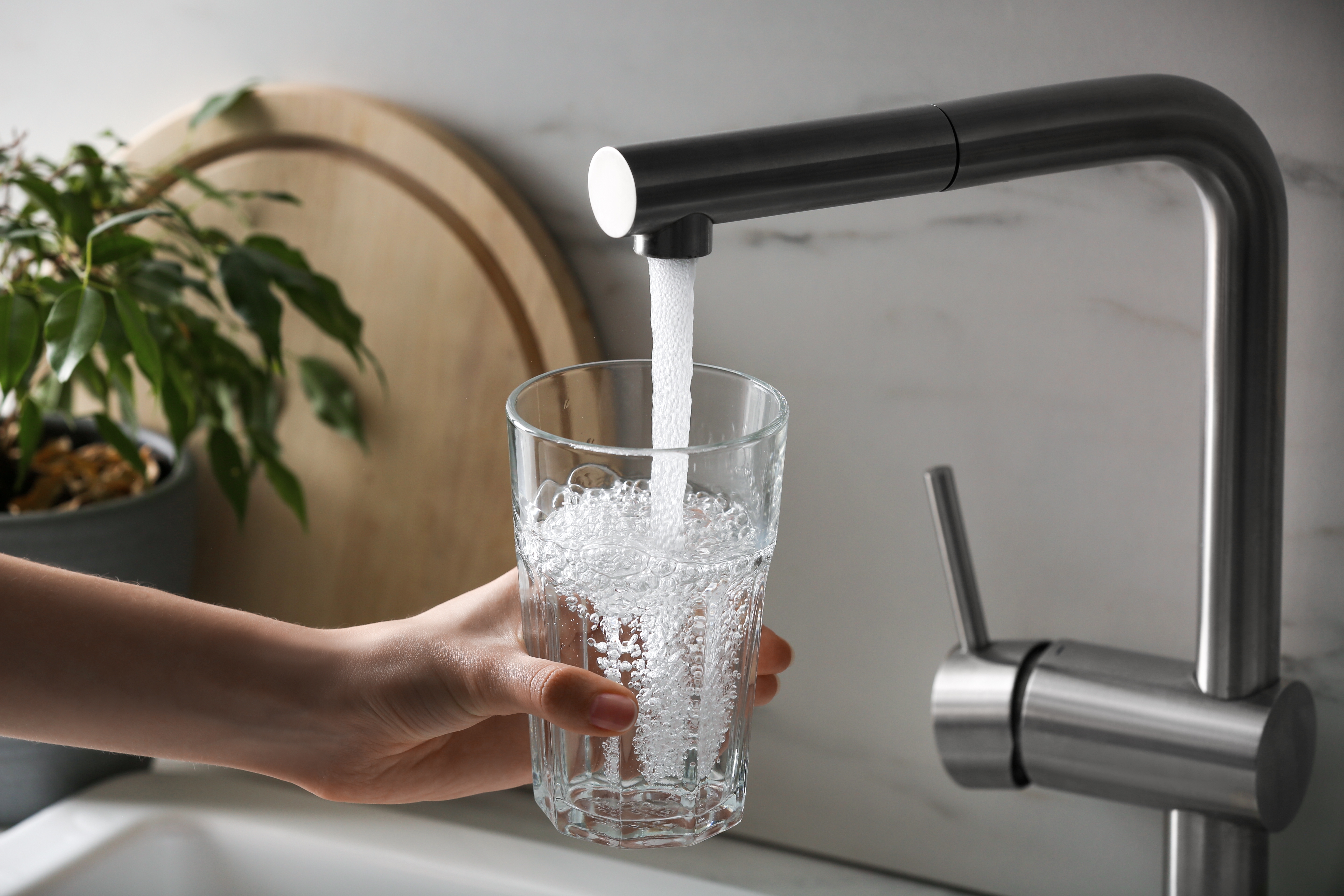 Een persoon vult een glas met water uit een moderne keukenkraan met zacht water van de Minimax waterontharder.