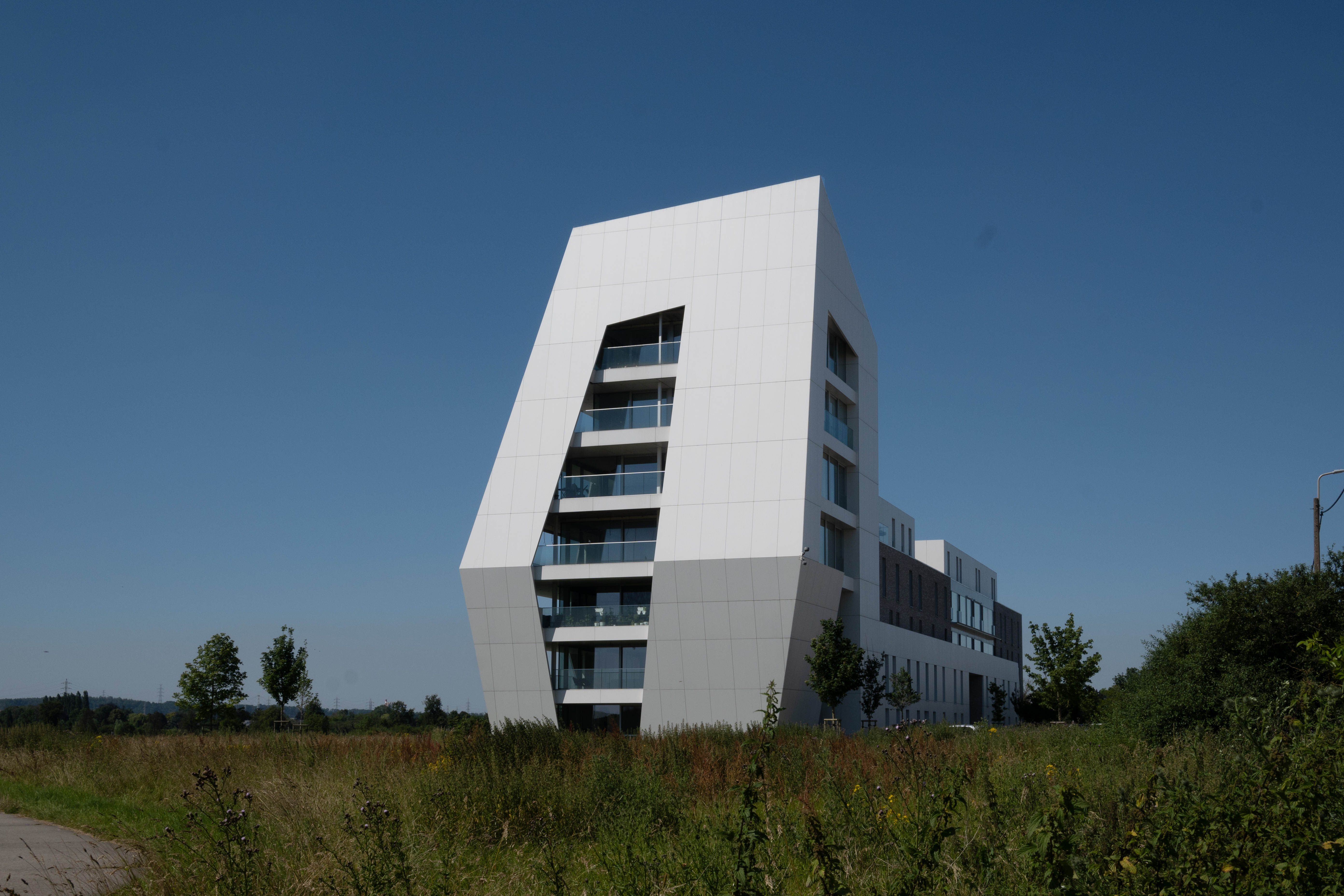 Bâtiment blanc moderne à façade inclinée situé dans un environnement verdoyant sous un ciel bleu, siège de l’adoucisseur d’eau Minimax à Oupeye.