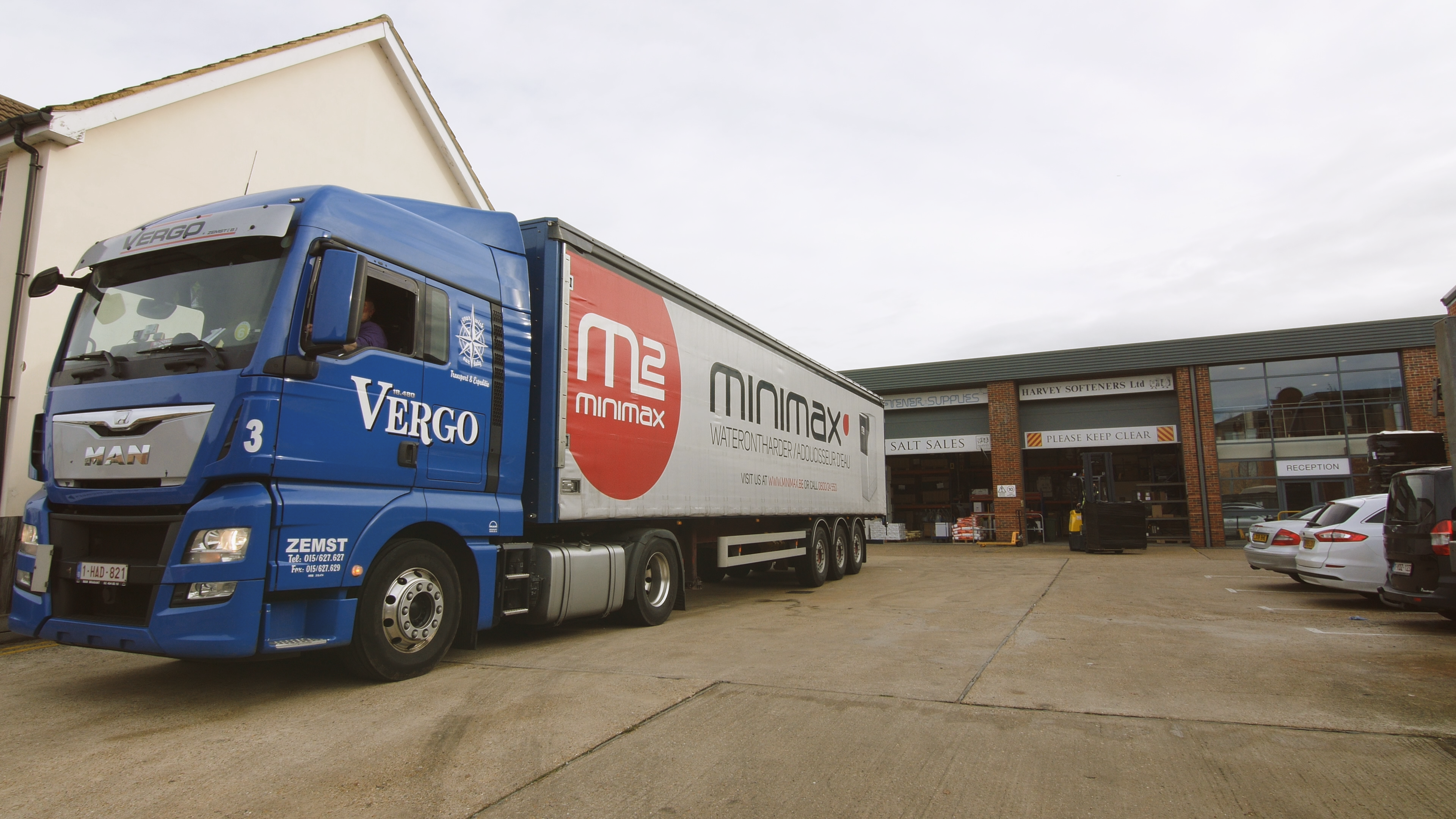 Camion Vergo avec logo Minimax garé devant un bâtiment portant les textes « Harvey Softeners Ltd » et « Salt Sales ».