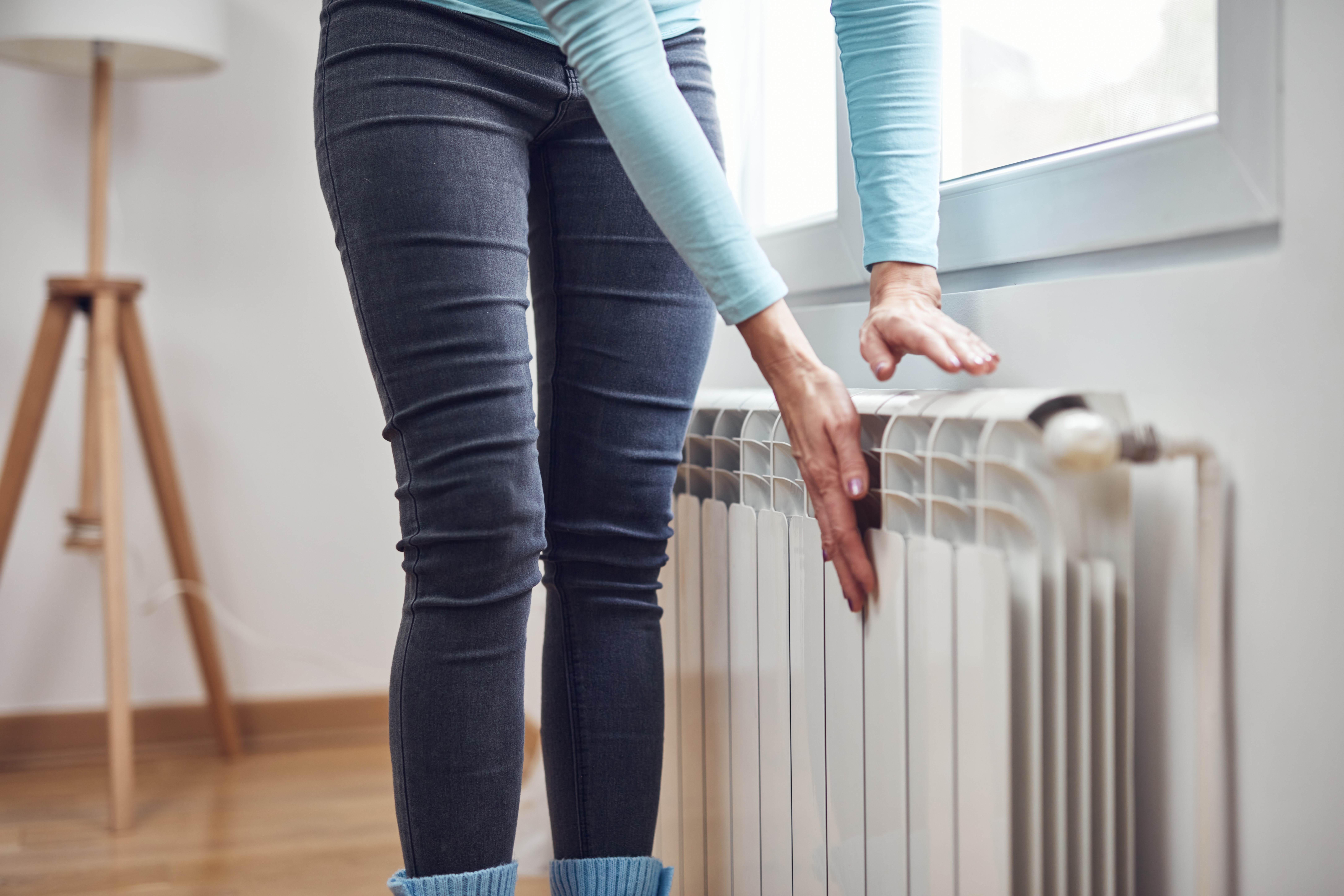 Femme vêtue de bleu debout près d’un radiateur, tendant les mains vers la chaleur grâce à l’adoucisseur d’eau Minimax.