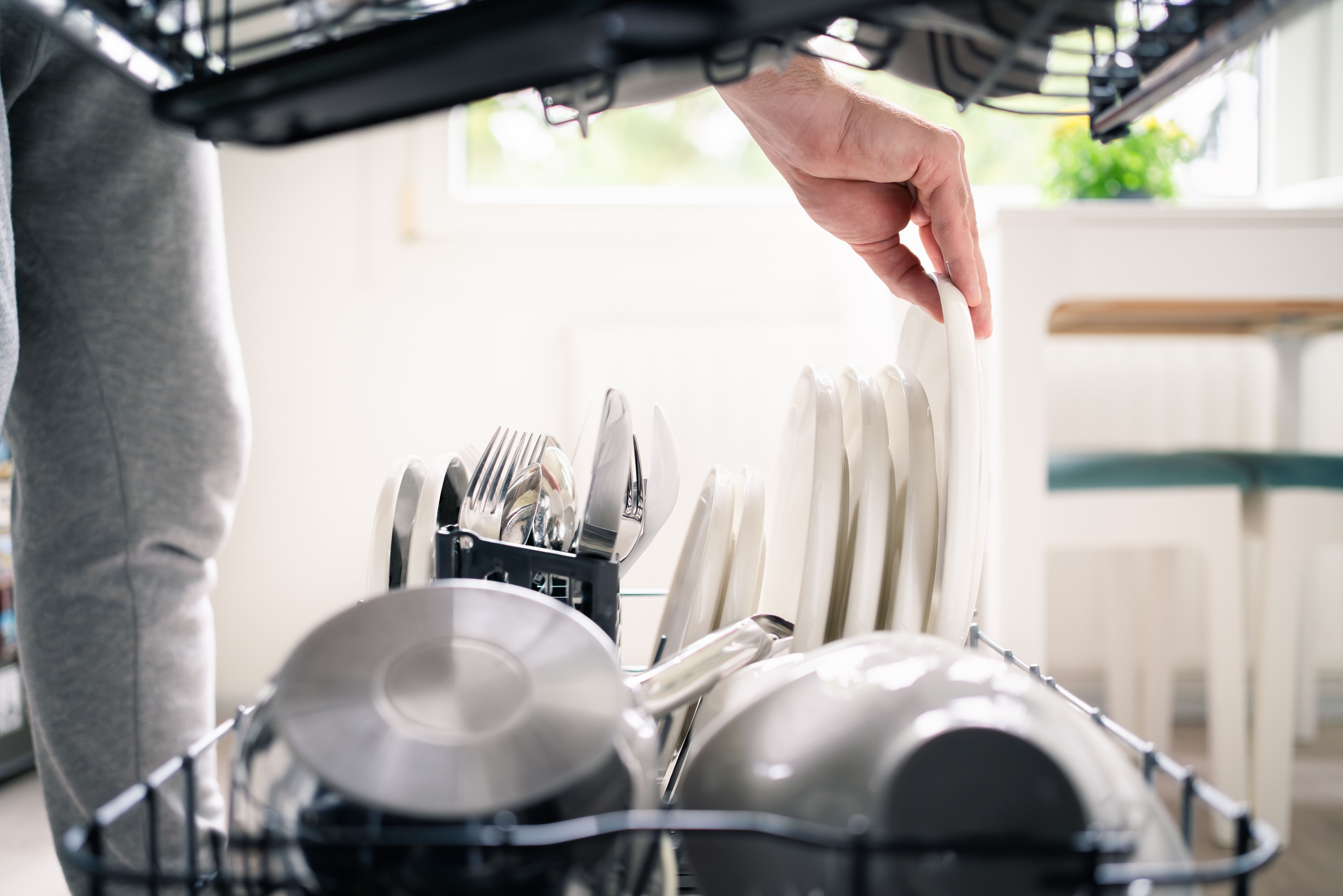 Gros plan sur une personne chargeant un lave-vaisselle avec assiettes et casseroles grâce à l’adoucisseur d’eau Minimax.