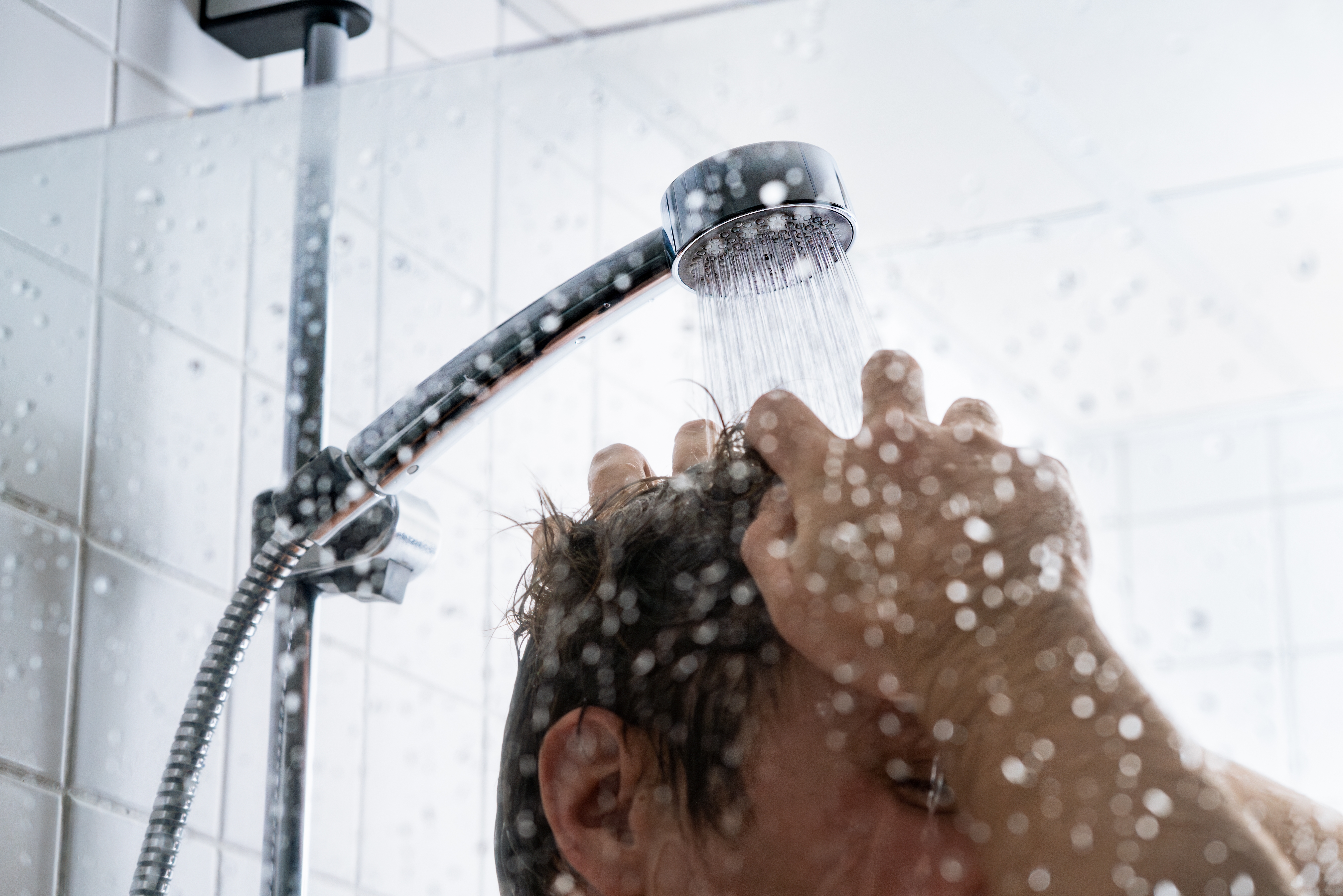 Persoon neemt een douche met stromend water uit een douchekop met zacht water van de Minimax waterontharder.