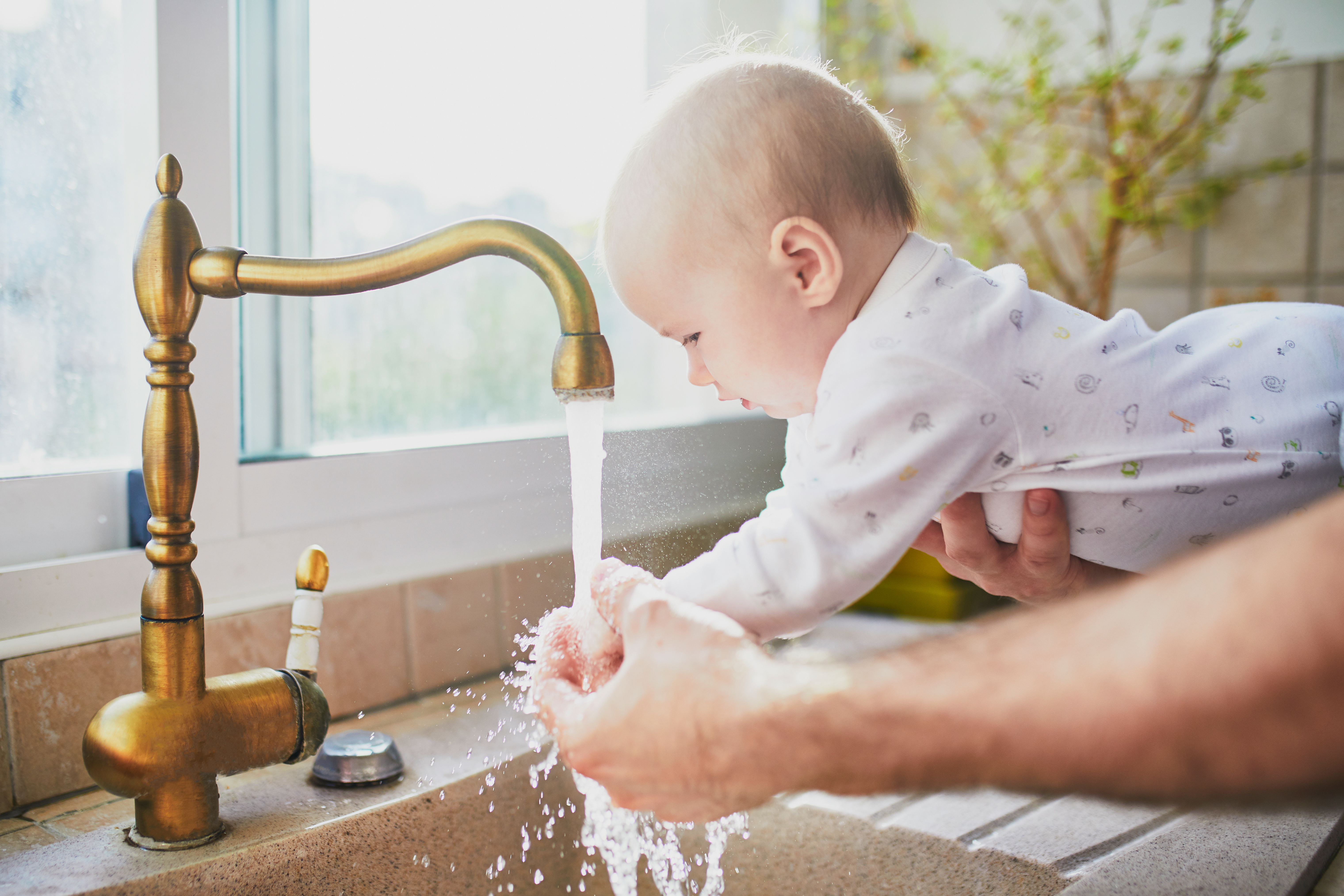 Een baby wast zijn handen onder een stromende kraan terwijl een volwassene helpt met zacht water van de Minimax waterontharder.