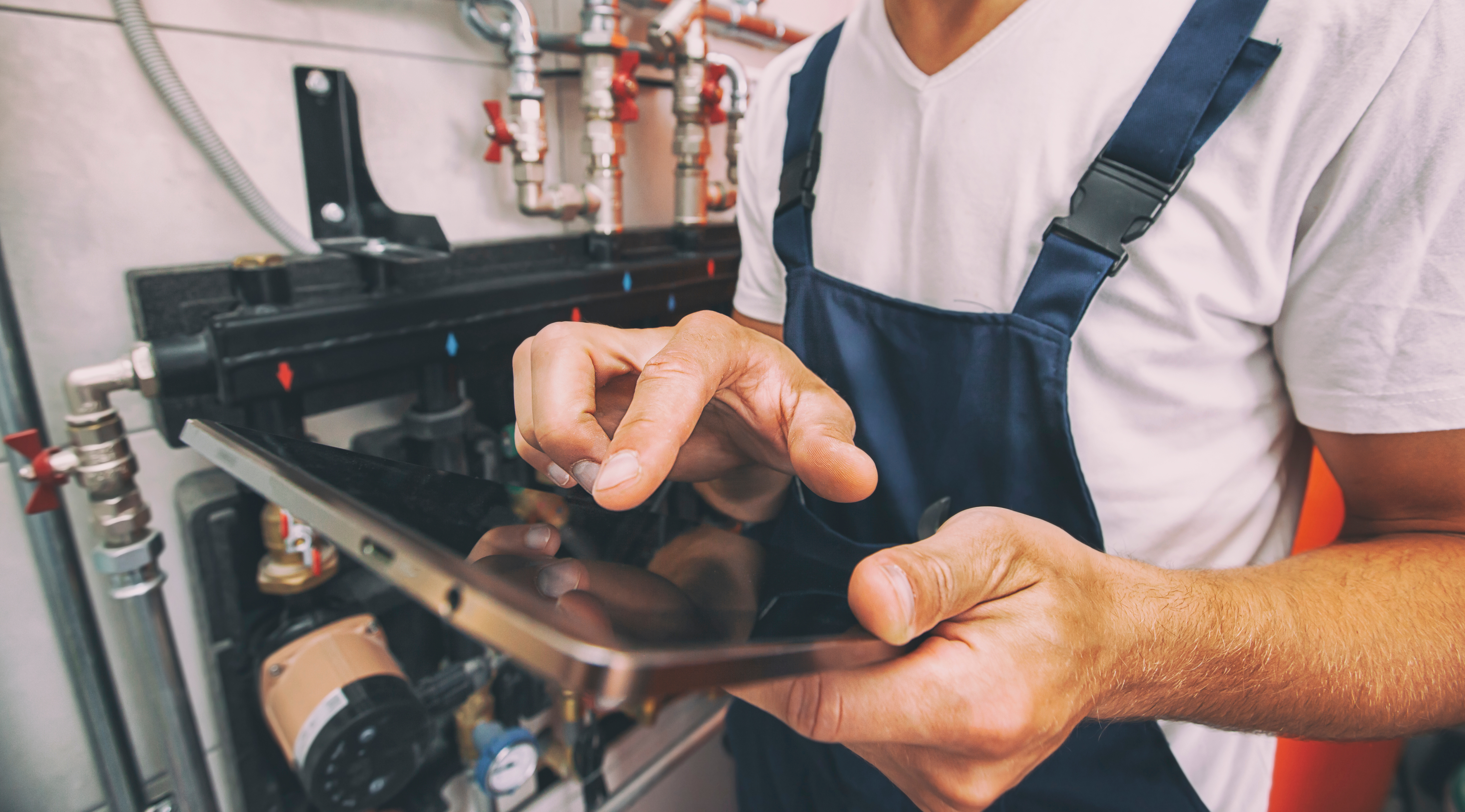 Technicien en salopette travaillant avec une tablette pour diverses techniques dans une habitation.
