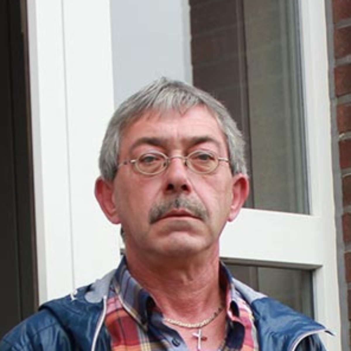 Een man met een snor en bril staat voor een raam van een bakstenen gebouw als tevreden gebruiker van de Minimax waterontharder.